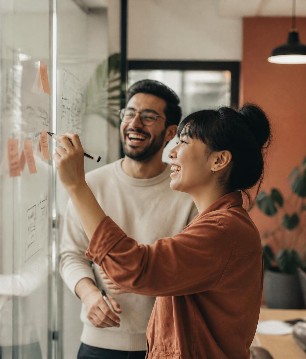 Two Tinkery teammates sketching ideas on a glass whiteboard.